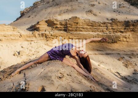 Brown-haired woman in purple glittering dress dancing on sand slope Stock Photo