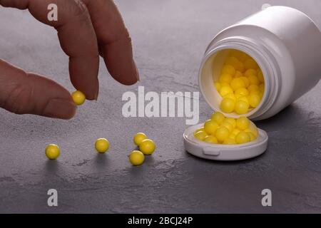 Close-up of opened white plastic medicine bottle lying on side and full of small round yellow pills of Vitamin C. Few pills are scattered over surface Stock Photo
