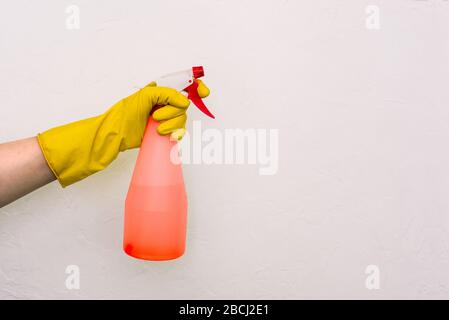 Worker's hand in a yellow glove with a red spray gun on a white background. Protection against germs, bacteria and viruses. Prevention of infectious d Stock Photo