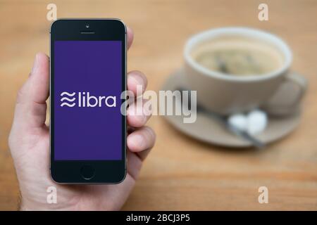 A man looks at his iPhone which displays the Facebook Libra logo (Editorial use only). Stock Photo