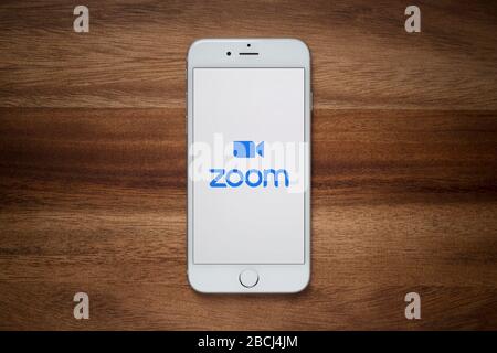 An iPhone showing the Zoom video conferencing website rests on a plain wooden table (Editorial use only). Stock Photo