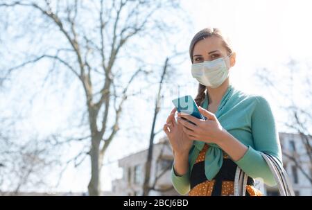 Woman using her phone wearing mask reading news about Covid-19 Stock Photo