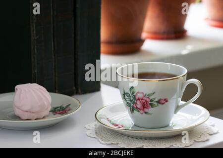 Tea in a vintage cup, marshmallows on a vintage saucer and old books on a light background. Stock Photo