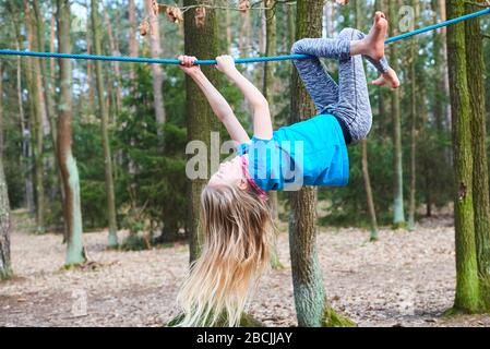 Young child girl hanging on rope upside down on playground in park Stock Photo