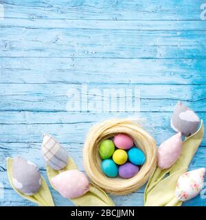 Textile tulip flowers and multi-colored wooden eggs in a nest on a blue background from wooden boards in a rustic style. Easter background for congrat Stock Photo