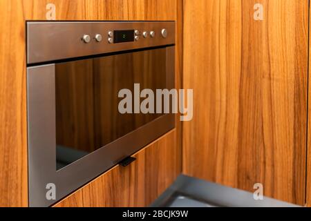 Modern wooden brown orange kitchen features cabinets with microwave oven on lower side and buttons closeup Stock Photo
