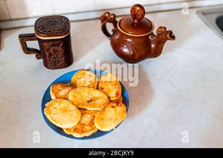 Rustic vintage antique traditional teapot and mug from Carpathian region of Ukraine with plate of fried cottage cheese pancakes on table Stock Photo