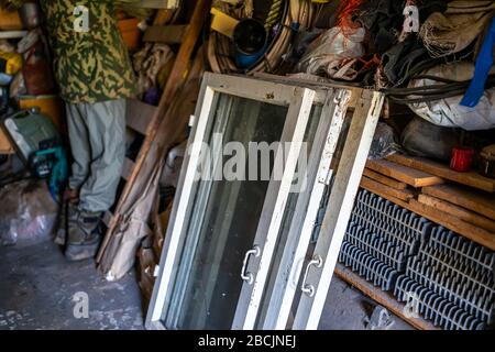 Person man standing inside garage workshop storage room with old glass cold window frames for garden in Ukraine dacha Stock Photo