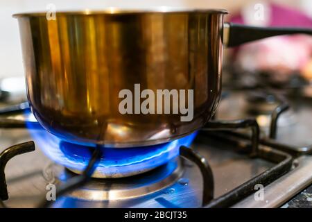 Macro closeup of gas stove top with blue fire flame and stainless steel pot with reflection and blurry blurred background Stock Photo