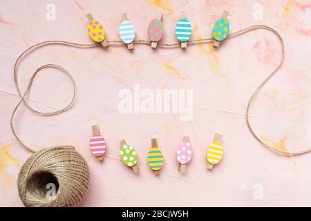 Pastel and gold colored eggs decoration pinned on a rope on a pastel pink background. Easter celebration concept. Top view, flat lay, copy space Stock Photo