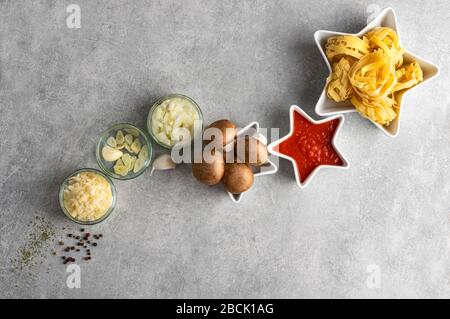 Dried pasta, mushrooms and vegetables on stone grrey background table top view, with copy space. Concept star composition tagliatelle and vegan bologn