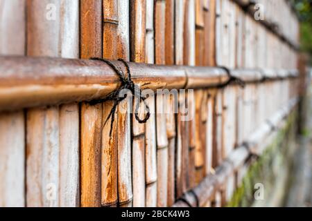 Kyoto, Japan residential area with closeup of bamboo wooden fence with red orange brown color by sidewalk with string or rope tied by Japanese garden Stock Photo