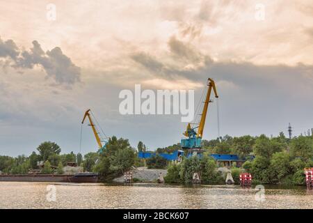 Industrial site with cranes on the bank of the Dnieper River to the close to the city of Zaporozhye, Ukraine. Stock Photo