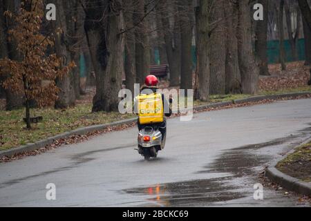 Kiev, Ukraine - February 27, 2020: Man from a delivery service from the yellow bag rides on a motor scooter on the street Stock Photo