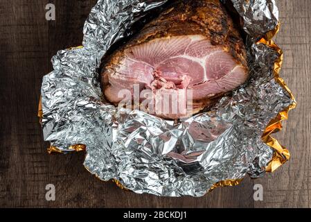 Spiral cut glazed and cooked ham in a foil wrapper on a wood table Stock Photo