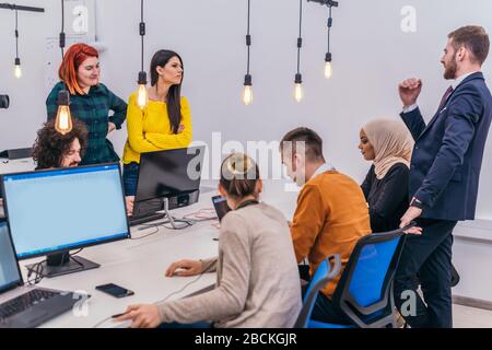 Handsome young executive explaining new employees an online task on theirs computers Stock Photo