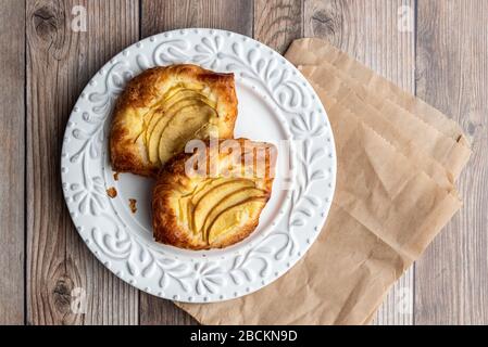 Fresh individual apple tarts on a white plate, brown paper sacks, wood background Stock Photo