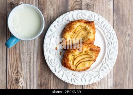 Fresh individual apple tarts on a white plate, blue cup of milk, wood background Stock Photo