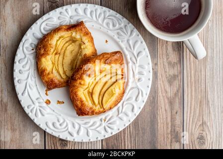 Fresh individual apple tarts on a white plate, cup of hot tea, wood background Stock Photo