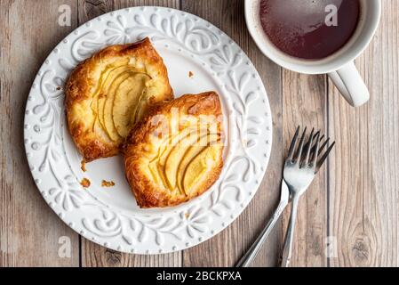 Fresh individual apple tarts on a white plate, forks, cup of hot tea, wood background Stock Photo