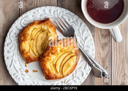 Fresh individual apple tarts on a white plate, forks, cup of hot tea, wood background Stock Photo