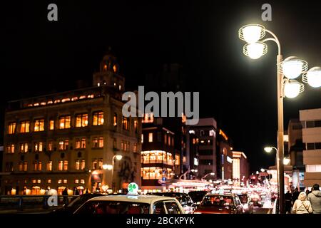 Kyoto, Japan - April 9, 2019: Street bridge near Gion district at night with illuminated buildings and cars traffic cab in evening with people walking Stock Photo