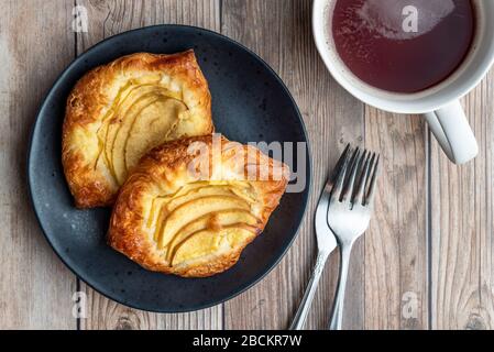 Fresh individual apple tarts on a black plate, forks, cup of hot tea, wood background Stock Photo