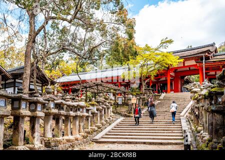 Nara, Japan - April 14, 2019: Kasuga taisha shrine row of stone lanterns on road street stairs up in spring with many people by entrance of red buildi Stock Photo