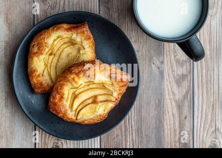 Fresh individual apple tarts on a black plate, mug of cold milk, wood background Stock Photo