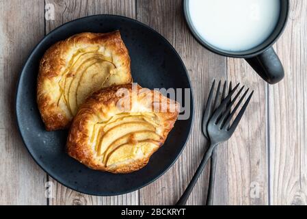 Fresh individual apple tarts on a black plate, forks, mug of cold milk, wood background Stock Photo