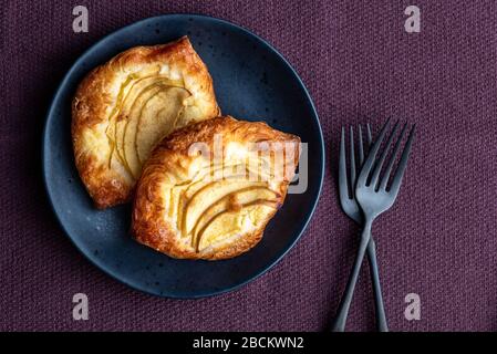 Fresh individual apple tarts on a black plate with forks, purple cloth background Stock Photo