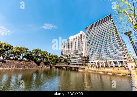 Tokyo, Japan - April 1, 2019: Palace Hotel building view of lake or pond water in modern downtown with cherry blossom trees in spring, people walking Stock Photo