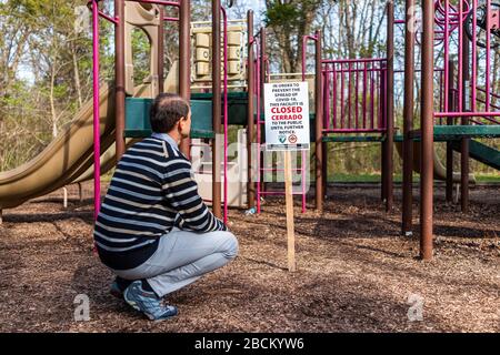 Herndon, USA - March 24, 2020: Man looking at children's playground sign in Fairfax Virginia city for park facility closure, closed to public due to c Stock Photo