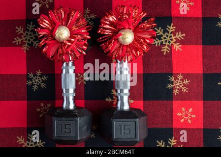 Holiday fitness, pair of 15-pound dumbbells on a holiday background of red and black with gold snowflakes, red and gold bows Stock Photo