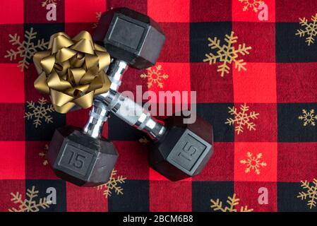 Holiday fitness, pair of 15-pound dumbbells on a holiday background of red and black with gold snowflakes, gold bow Stock Photo