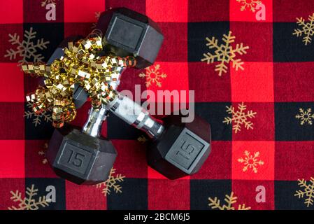 Holiday fitness, pair of 15-pound dumbbells on a holiday background of red and black with gold snowflakes, gold ribbon Stock Photo