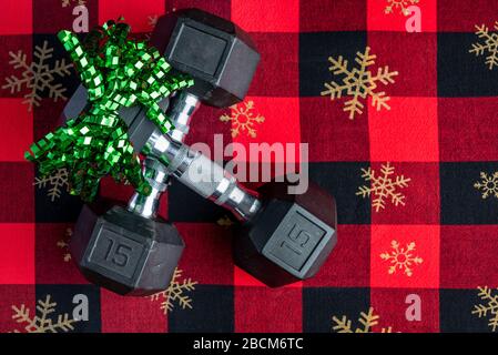 Holiday fitness, pair of 15-pound dumbbells on a holiday background of red and black with gold snowflakes, green ribbon Stock Photo