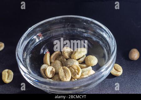 Close-up shot of green unroasted coffee beans, in a small glass bowl on a black background Stock Photo