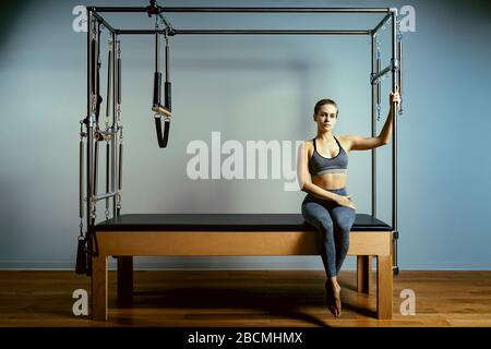A young girl does Pilates exercises with a bed reformer, barrel