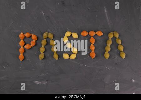 The words PASTA drawn with a kind of pasta, conchiglie. Textured Italian food background concept. Top view flat lay close-up Stock Photo