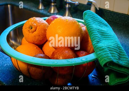 Freshly cleaned basket of citrus fruit rests in a basket on the kitchen counter next to stainless steel sink in a kitchen. Water droplets cling to the Stock Photo