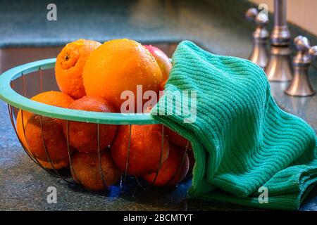 Freshly cleaned basket of citrus fruit rests in a basket on the kitchen counter next to stainless steel sink in a kitchen. Water droplets cling to the Stock Photo