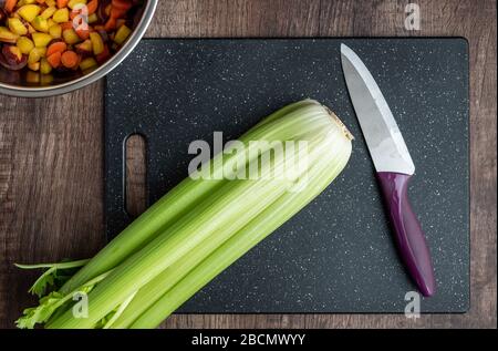 Bunch of celery washed and ready to chop on a black cutting board with chef knife Stock Photo