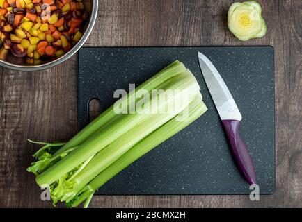 Bunch of celery washed and ready to chop on a black cutting board with chef knife Stock Photo