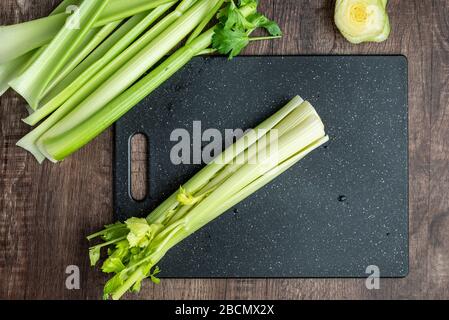 Celery stalks washed and ready to chop on a black cutting board, wood table Stock Photo