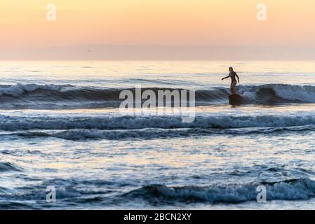 Young woman enjoying a pre-sunrise 'dawn patrol' surfing session at Jacksonville Beach, Florida. (USA)