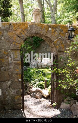 The arched stone gateway (guarded by a gargoyle) leading to the garden at the Hammond Castle Museum in Gloucester, Massachusetts, USA. Stock Photo