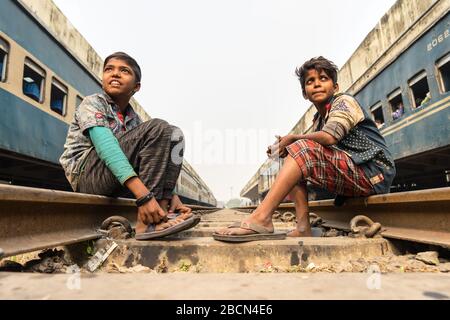 Dhaka / Bangladesh - January 19, 2019: Two young boys smile while sitting in the train tracks between two trains in Dhaka train station Stock Photo