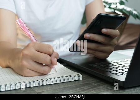 Young business woman sitting at table with laptop and taking notes in notebook. Stock Photo