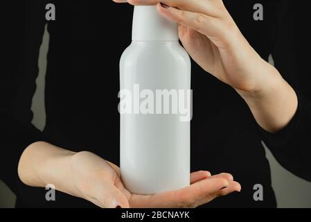Generic white bottle in female hands against low light backdrop. Product photography, blank plastic bottle with space for brand text or logo Stock Photo